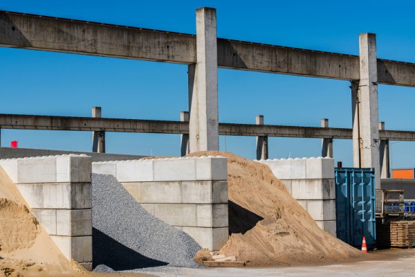 Large piles of sand and gravel are stored against concrete structures. The bright blue sky adds vibrancy to the industrial setting.